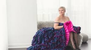 Bonnie Masina in a lavish, purple flamenco dress, seated on a couch.